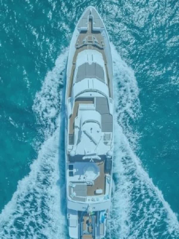 A motor yacht seen from directly above, cutting a white wake through turquoise water